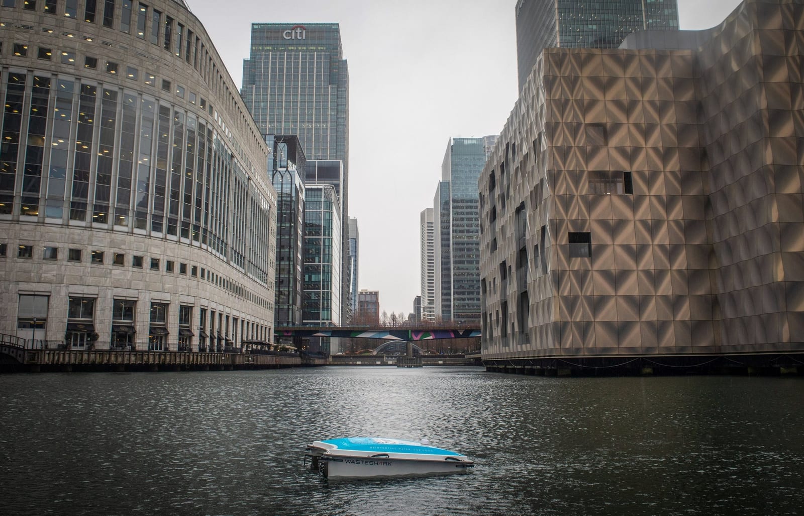 An Aqualibra branded WasteShark drone working a Canary Wharf dock, surrounded by office towers.