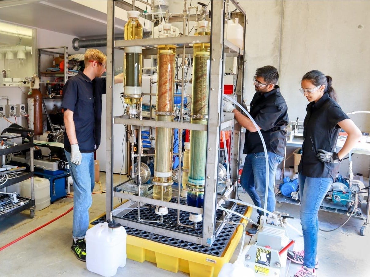 Three engineers running a pilot-scale filtration rig in a workshop