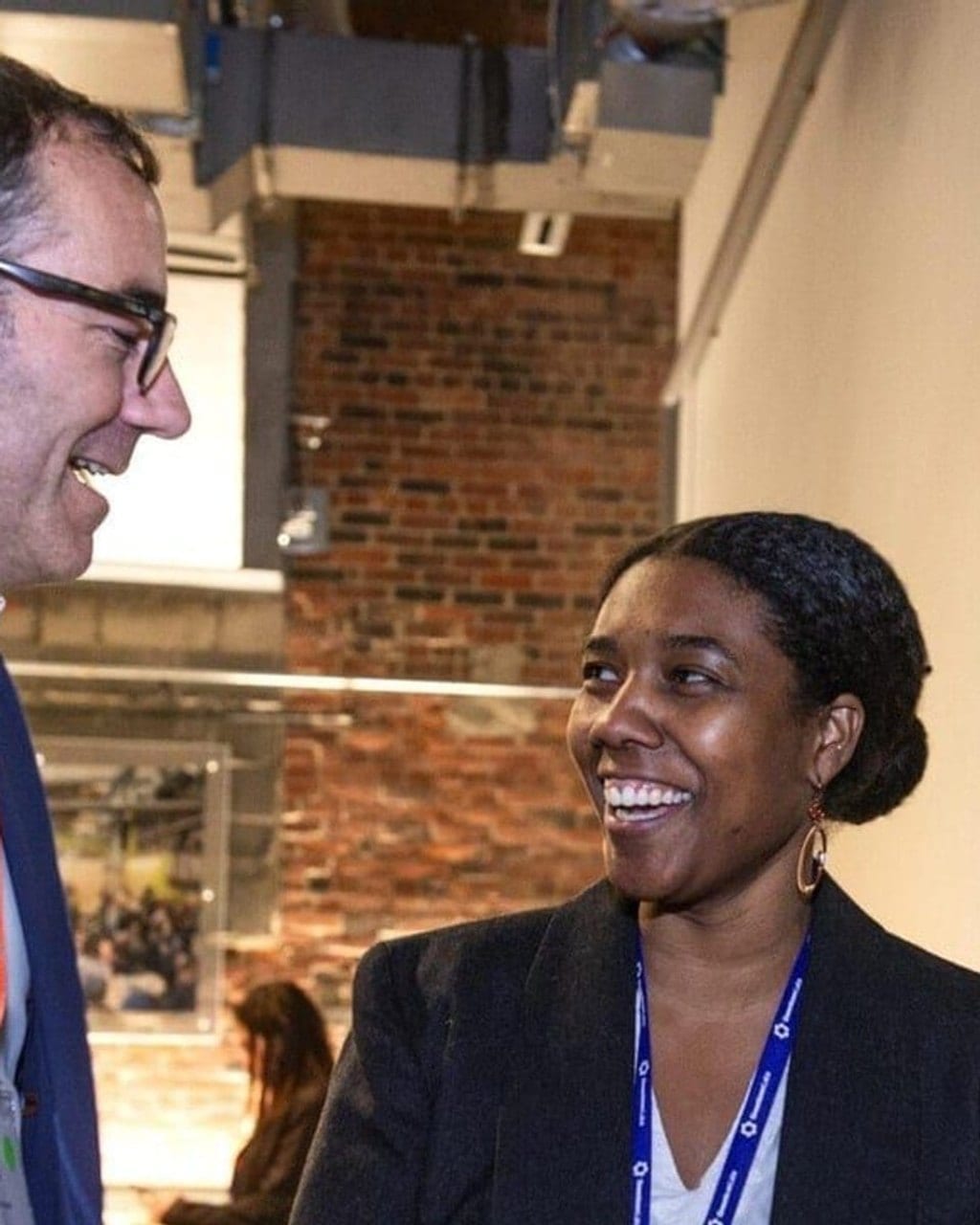 Two delegates laughing mid-conversation at a climate industry event, lanyards visible.