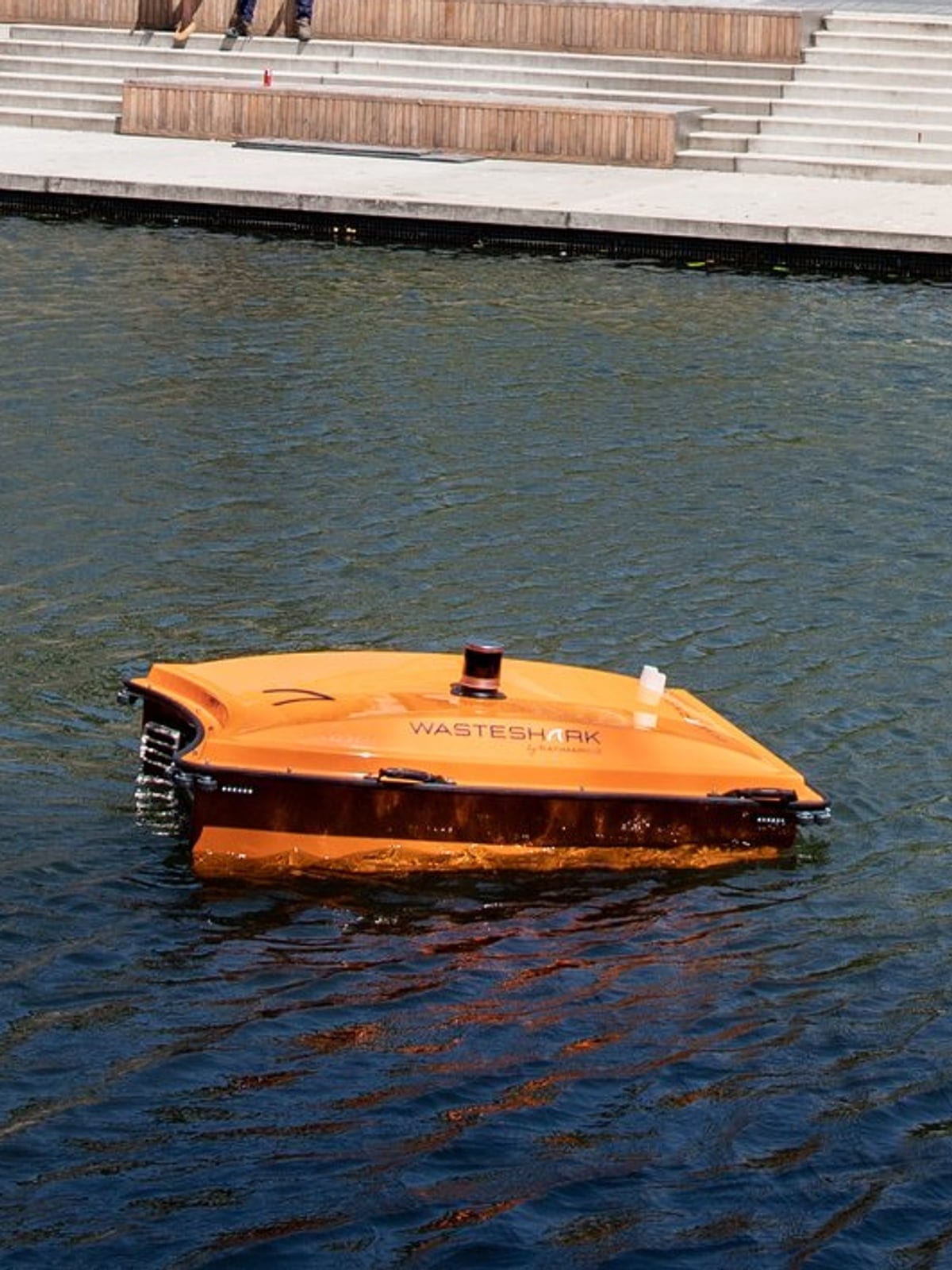 An orange WasteShark drone working a Rotterdam canal beside the quay steps.